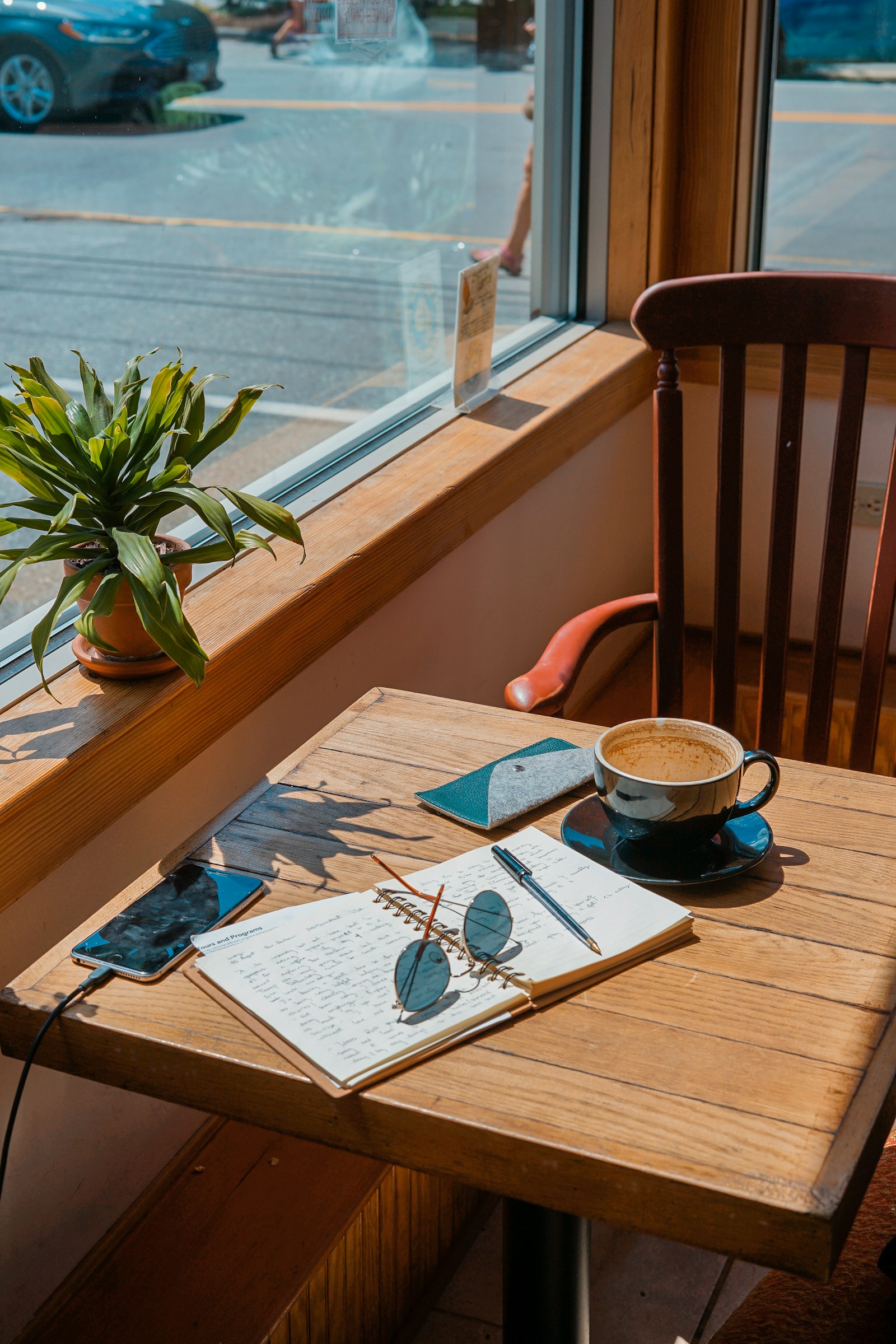 Un café et un carnet sur une table près d'une fenêtre